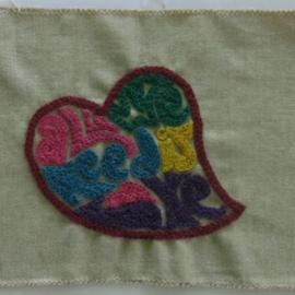 Fabric quilt square chain stitched with a heart and the the words all we need is love within the heart