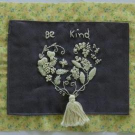Quilt piece embroidered with flowers and leaves in a heart with the words be kind